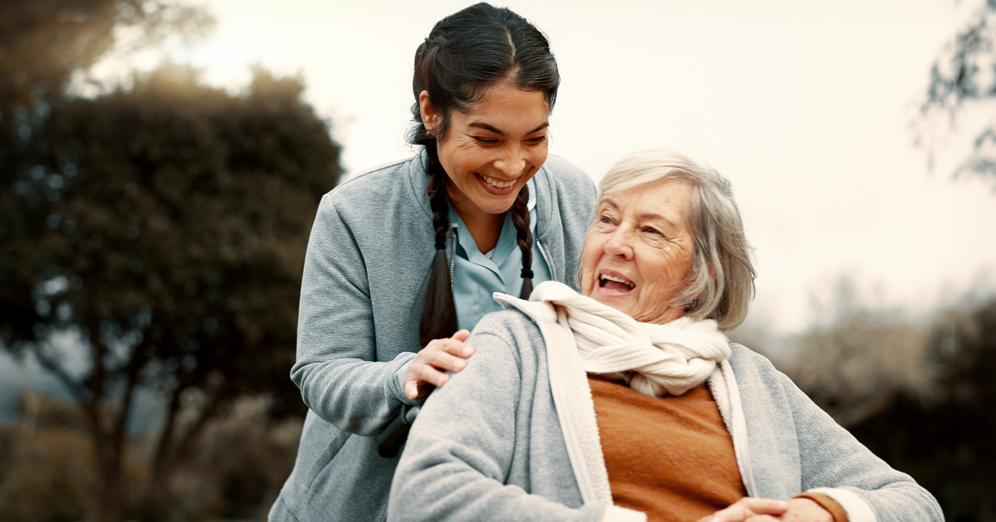 Senior woman, talking and outdoor with caregiver, nurse or healthcare service for person with a disability and wheelchair. Happy, face and elderly lady in park with care and support in retirement.
